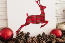22 a simple white sign with a plaid deer plus red ornaments and pinecones for a cool mantel