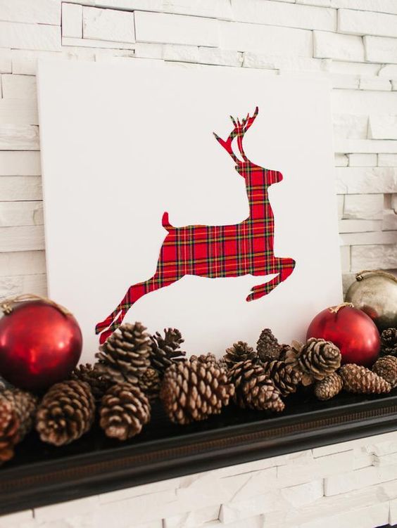 a simple white sign with a plaid deer plus red ornaments and pinecones for a cool mantel