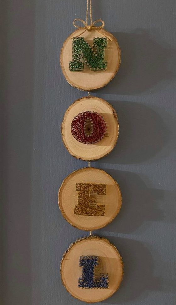 a creative Christmas decoration of tree slices and colorful string art letters is a cool idea instead of a wreath