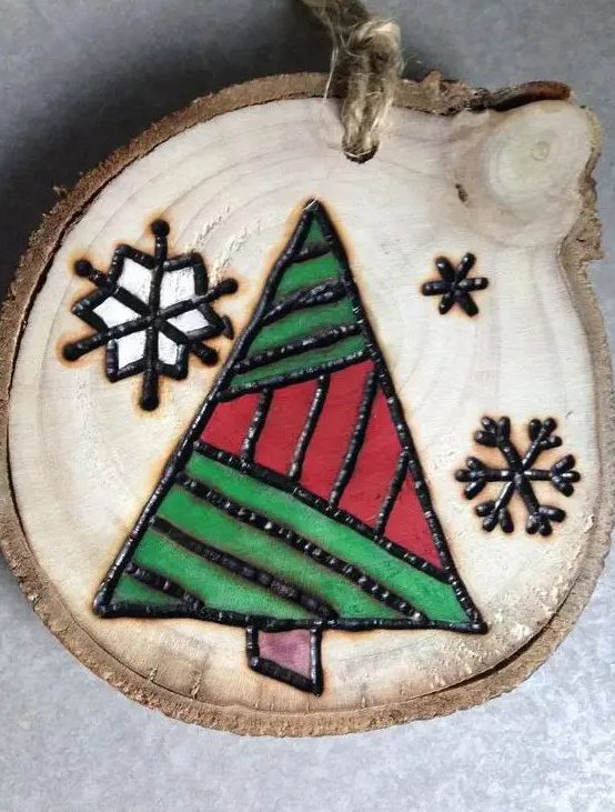 a wood burnt and painted Christmas ornament with snowflakes and a geometric tree