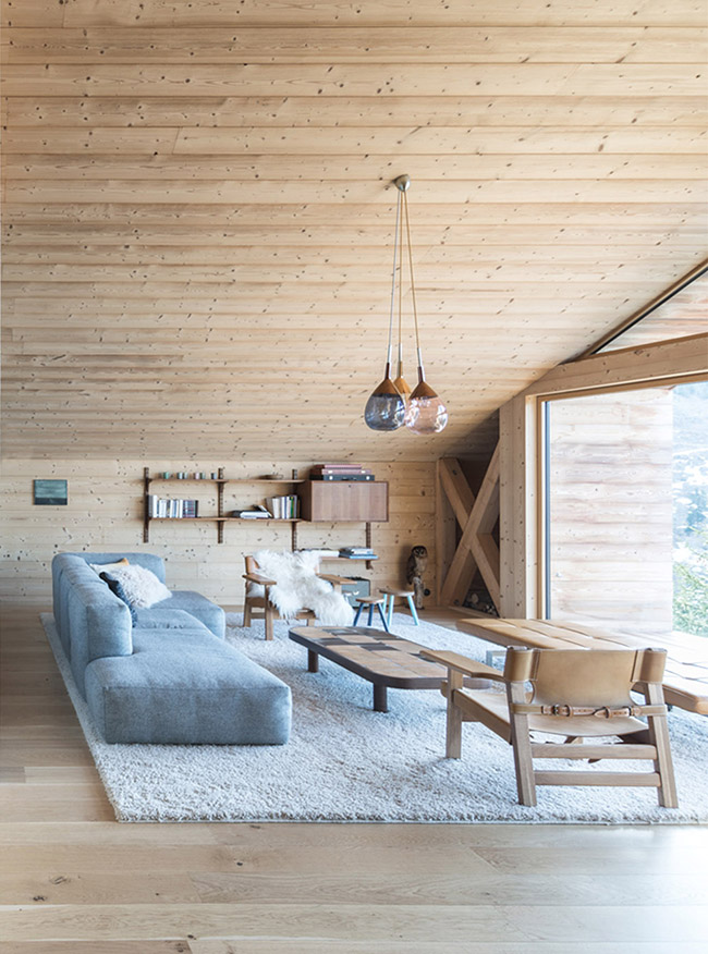 The room is fully clad with light-colored wood, the furniture is partly wooden too and there some wall shelves