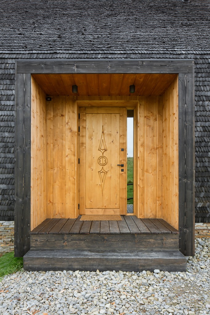 The house is clad with black shingles and the front door is light-colored with a carved decorative element