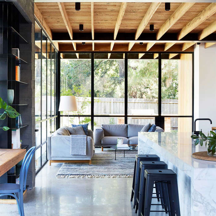 The living space is done with dove grey furniture, a wooden ceiling with beams and blackened metal all over the home