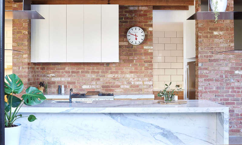 The kitchen features white cabinets, a marble kitchen island and exposed brick