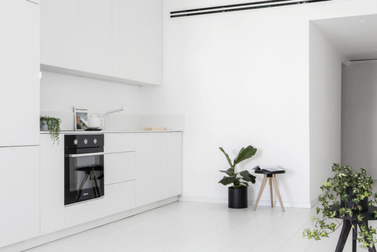 The kitchen is done with sleek white cabinets and lots of potted greenery enliven the minimalist space