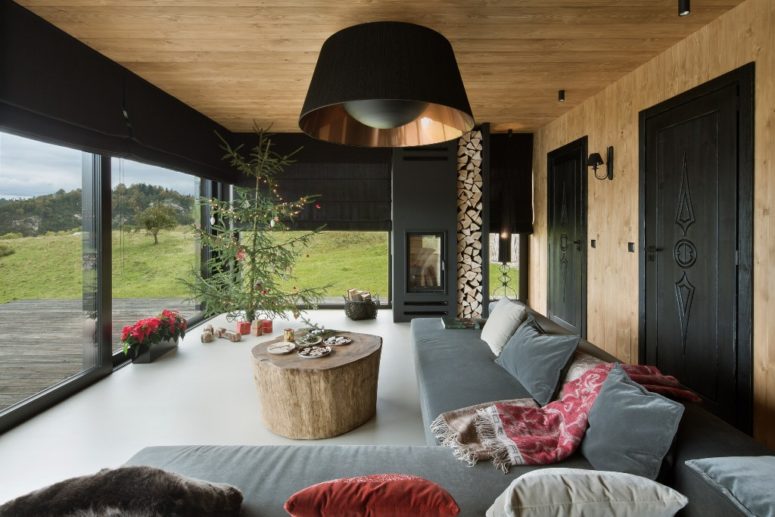 The living room features a hearth with firewood, a large grey corner sofa and a large tree stump table