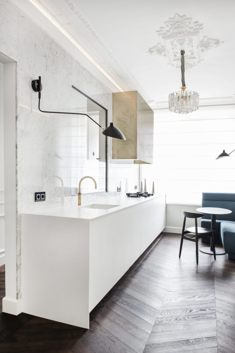 almost all white kitchen design The kitchen is done with a marble backsplash, a white cabinet, a hanging metallic one and a bold glam chandelier