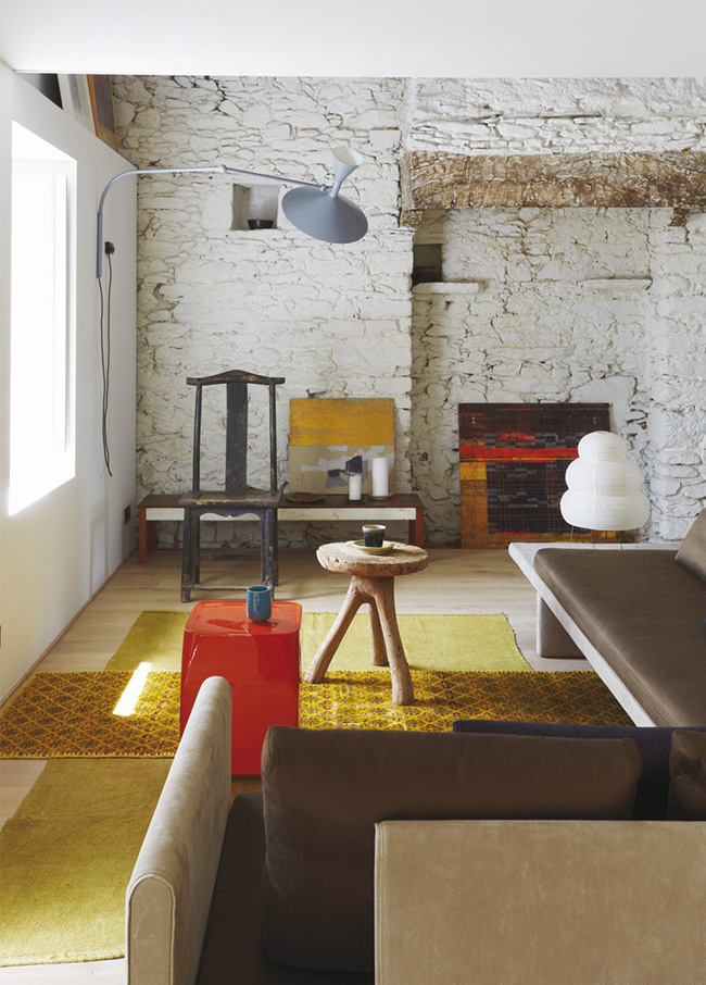 The living room features a whitewahsed stone clad, colorful textiles and furniture and reminds that the house is rather old