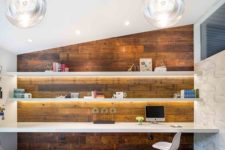 a modern home office with lit up floating shelves and a matching desk in fonrt of a reclaimed wood wall