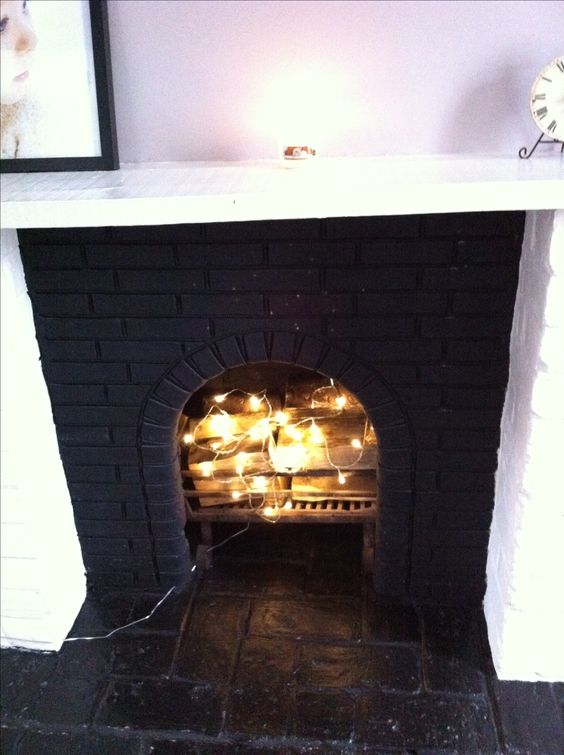 a faux fireplace clad with black brick and firewood and string lights inside looks super cool