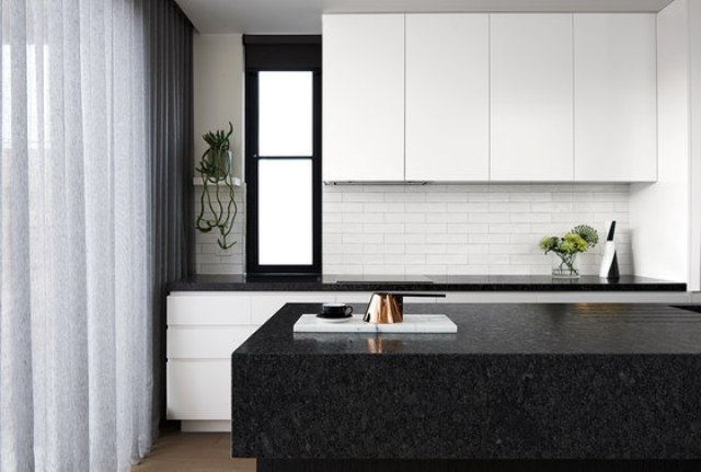 white kitchen with a black island The kitchen is done with white cabinets and black stone countertops, the backsplash is of white brick