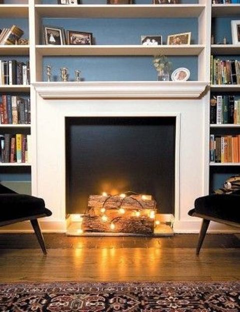 a faux fireplace with a black backdrop, some firewood covered with string lights in front of it