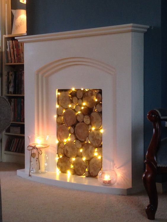 a non-working fireplace with wood slices and string lights in between them for a natural look
