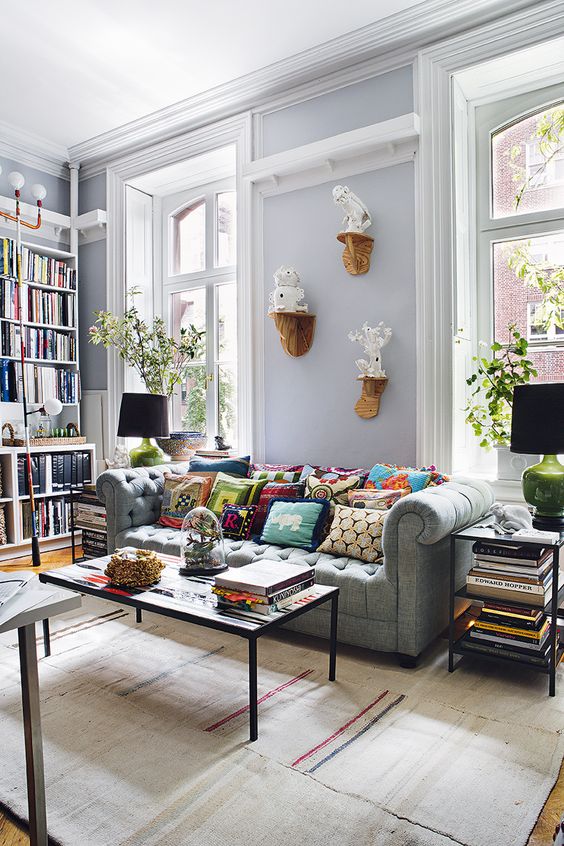 a cozy pastel living room with a light grey Chesterfield sofa and lots of books