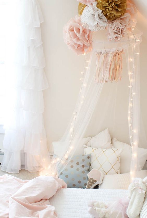 a sheer canopy with fabric pompoms and string lights is sure to make a girl's bed welcoming