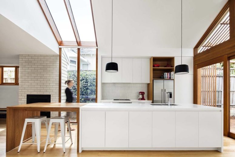 stylish white kitchen design with wooden elements The kitchen is done with sleek white cabinets, a brick clad fireplace, a white tile backsplash and black pendants