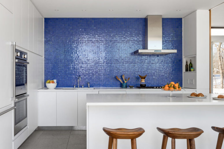 The kitchen is done with white cabinets and a kitchen island, and the backsplash wall is clad with purple tiles The kitchen is done with white cabinets and a kitchen island, and the backsplash wall is clad with purple tiles