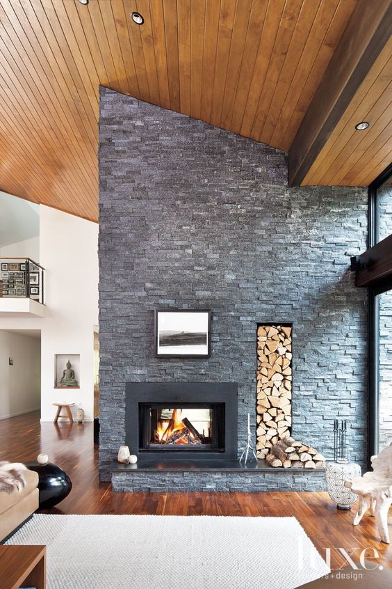 this faux stone wall with a built-in fireplace and firewood storage brings coziness and a bold touch