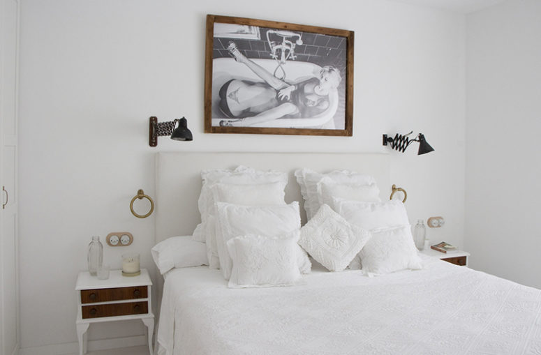 The master bedroom is spruced up with a cool artwork, vintage nightstands and a inviting bed with lots of pillows