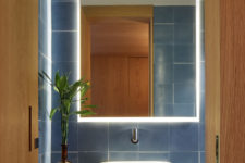 08 The powder room is done with blue tiles, a marble countertop and a sculptural sink and a lit up mirror
