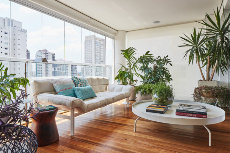 The terrace sitting space is done with a modern sofa, potted plants and greenery and a glazed wall that shows off a city landscape The terrace sitting space is done with a modern sofa, potted plants and greenery and a glazed wall that shows off a city landscape