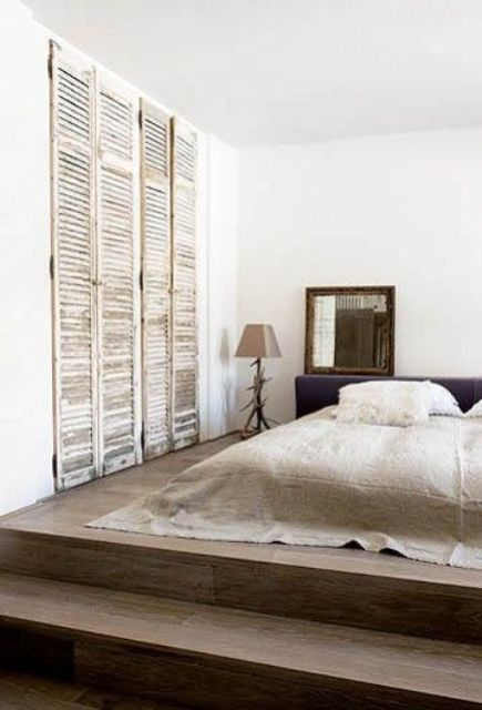 a minimalist sleeping space with old shutters as wardrobe doors that add texture and interesting to the space