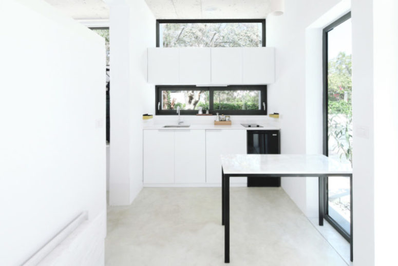 The kitchen features white cabinets and windows as a backsplash and over the cabinets to fill the space with light