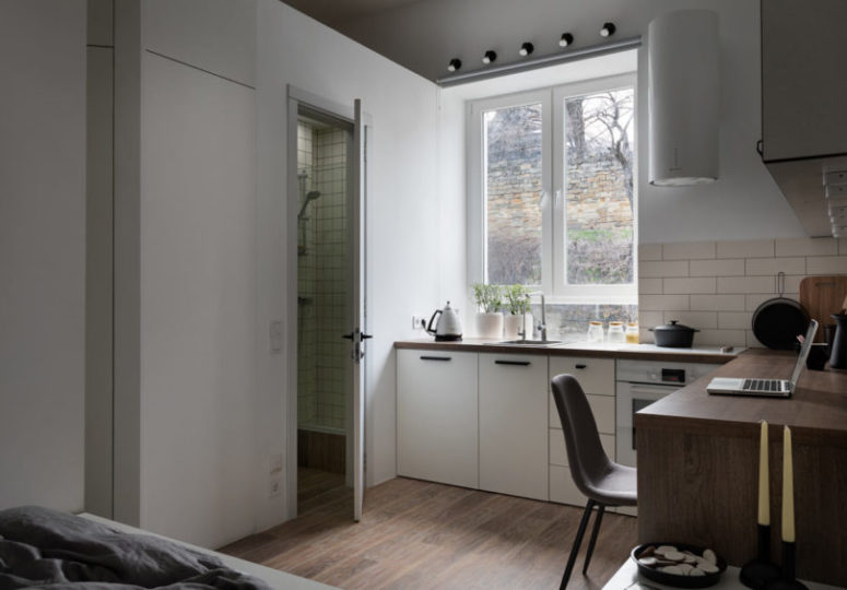 There's a large window and a tiny bathroom space clad with off-white tiles
