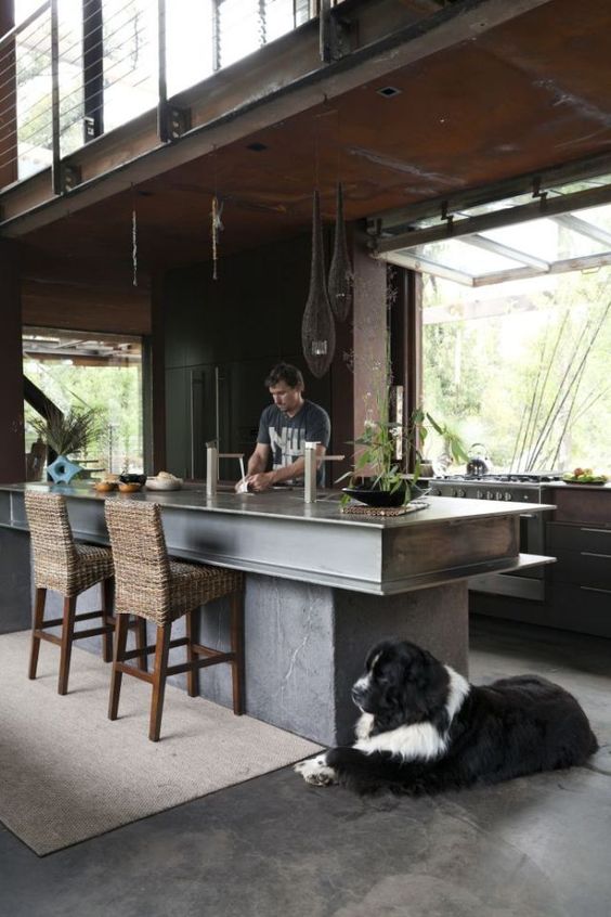 a large concrete and metal kitchen island features much storage space and a breakfast space, too