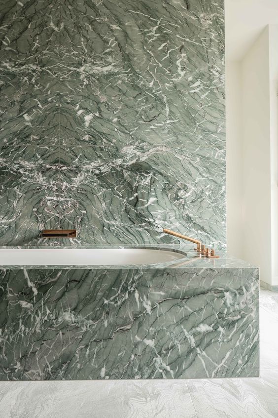 a green marble wall and a covered bathtub with brass fixtures create a really refined and luxurious space