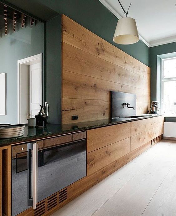 a modern kitchen with sleek walnut cabinets and a backsplash and dark green walls