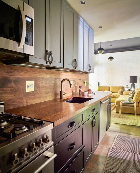 a navy and light blue kitchen with leather handles and a rich-colored plywood backsplash and countertop