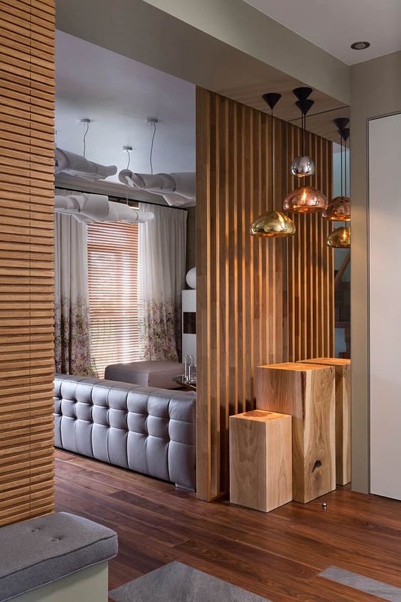 a vertical wooden plank screen separates the entryway and the living room making the conversation pit more private