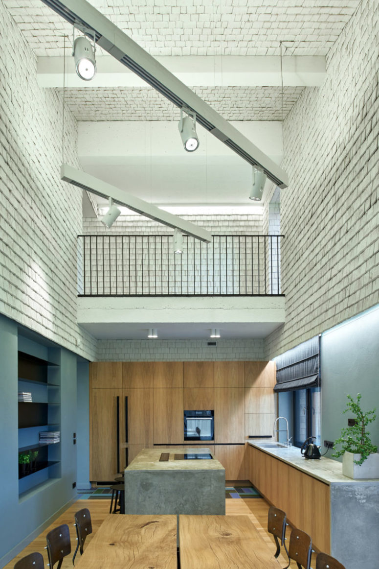 The kitchen is done with light-colored wooden cabinets, and the same wood is used for the dining table