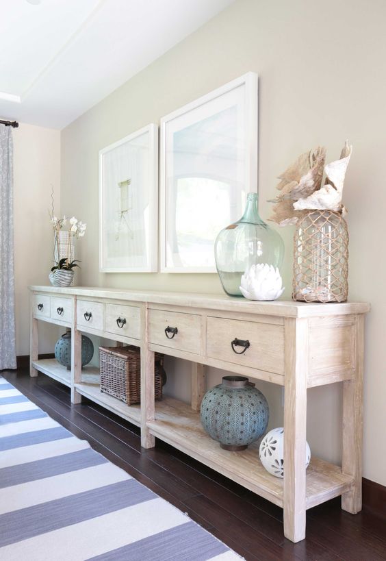 a long whitewashed console with sea-inspired artworks, large bottles and lanterns and shells