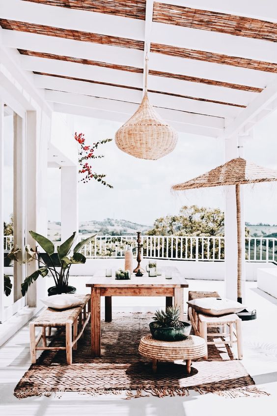 a boho porch dining space with a wooden set, woven benches and ottomans and hanging lamps