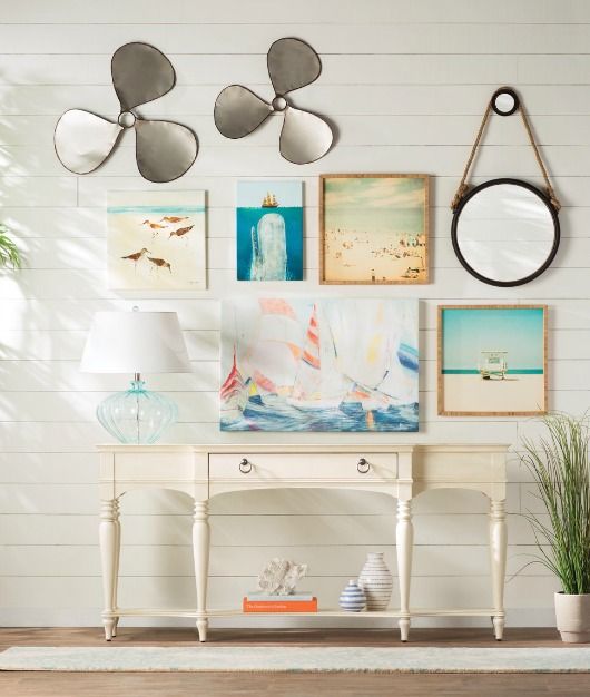 a coastal entryway with a gallery wall of artworks, a white vintage console, a mirror and some screws