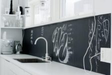07 a minimalist white kitchen with a chalkboard backsplash that helps it stand out and look more interesting