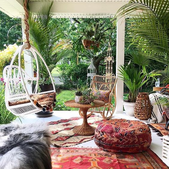 a boho porch with printed and colorful textiles, woven lanterns and baskets, rattan furniture and potted greenery