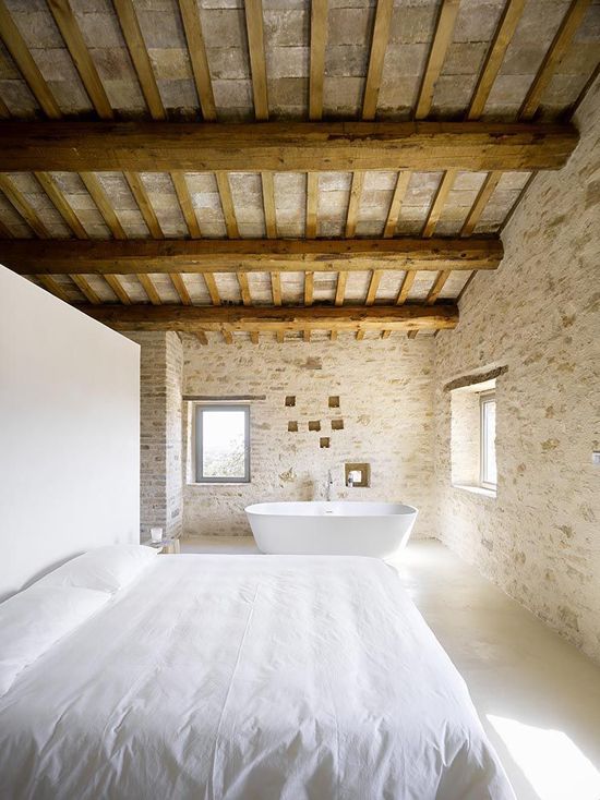 a rural Provence bedroom with much stone and wood and a bathtub by the window to enjoy the views