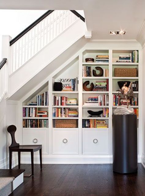 a cozy under stairs reading nook with a built-in bookcase, a chair and a sculpture