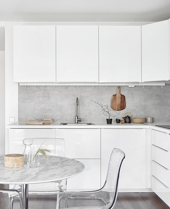 a white Scandinavian kitchen is spruced up with a concrete countertop and acrylic chairs