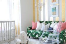12 a bright nursery with a glam feel, a striped gold and white wall and ceiling, a tropical leaf print sofa and an acrylic chair
