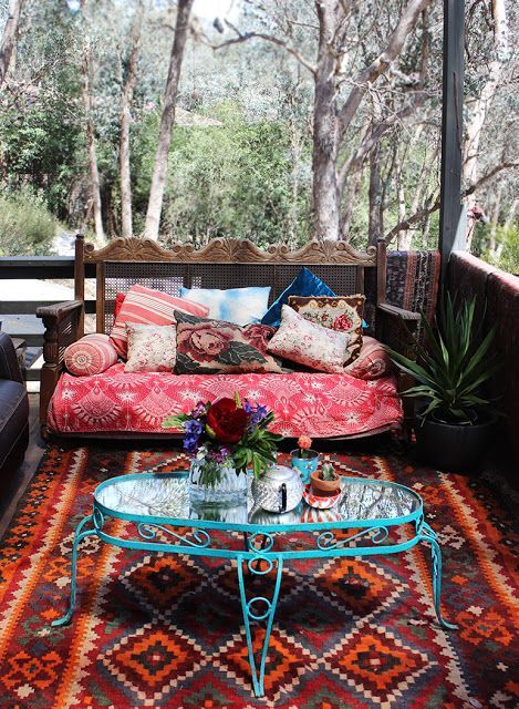 a gypsy-styled porch with a bright printed rug, a colorful bench and a blue forged side table
