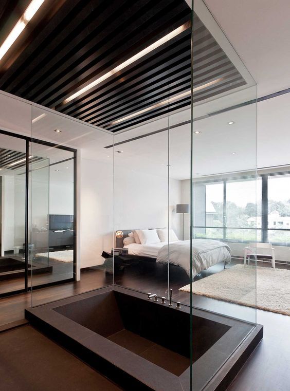 a contemporary bedroom with a large dark metal sunken bathtub separated with glass to avoid splashes on the floor