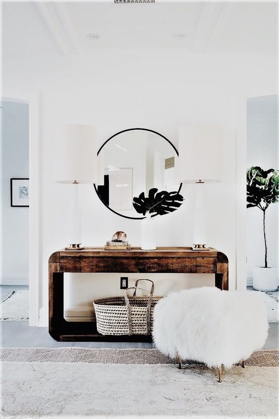 a rough wood console table, a round mirror, a faux fur stool and tropical leaves