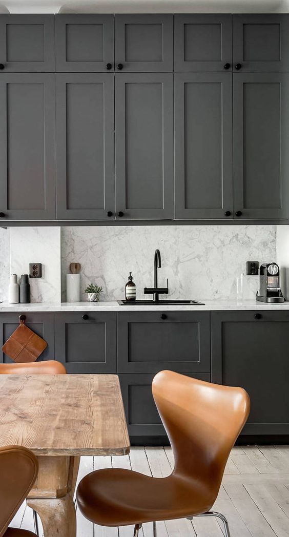 graphite grey cabinets contrast with a grey and white marble backsplash and countertops plus a black faucet