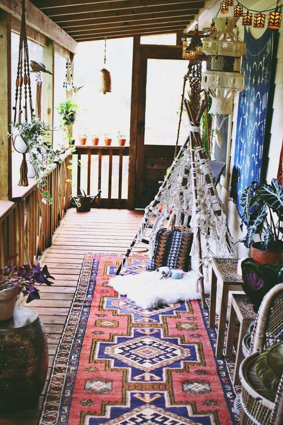 a boho porch with a printed rug, a teepee with macrame, lanterns, potted greenery plus rattan stools