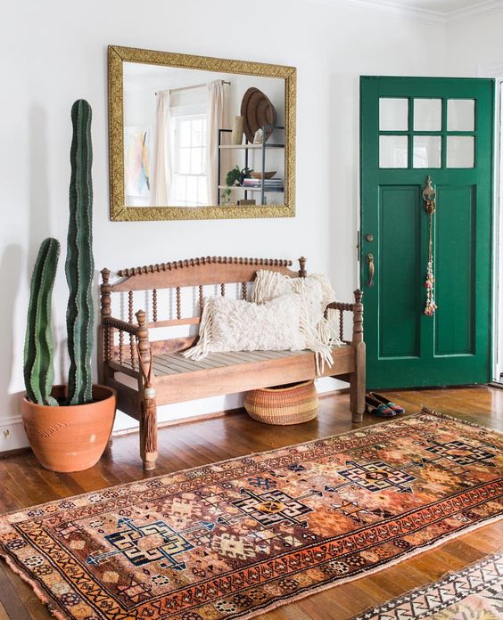 a boho rug, a vintage wooden bench, cacti and a mirror ina  gilded frame