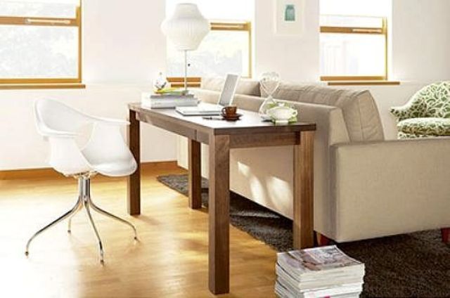 a narrow wooden desk placed behind the sofa and a chair plus a lamp that match the organic decor